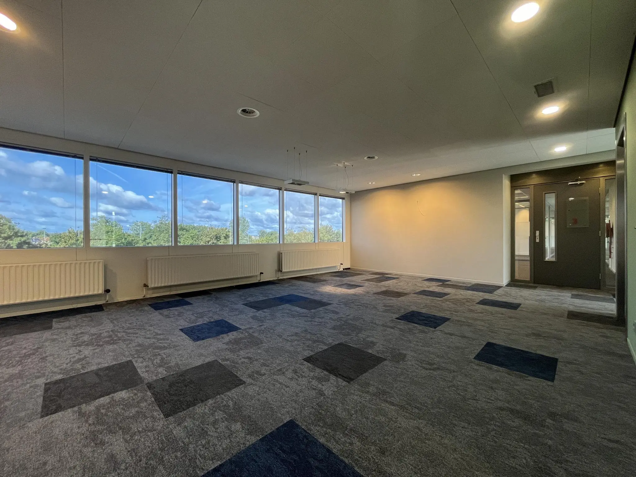 Leeg kantoorruimte met grote ramen, uitzicht op groen en blauw tapijt op de Baarnsche Dijk.